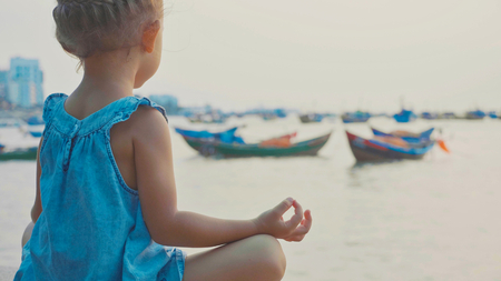 Little cute girl meditates in turkish pose at seafrontの写真素材