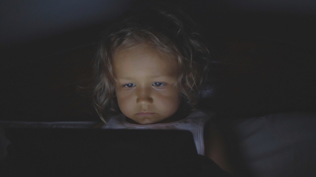 Portrait of little child girl using tablet technology in bed by night at home.の写真素材