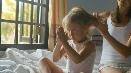 Young mother sits on the bed and combing her daughter.の写真素材