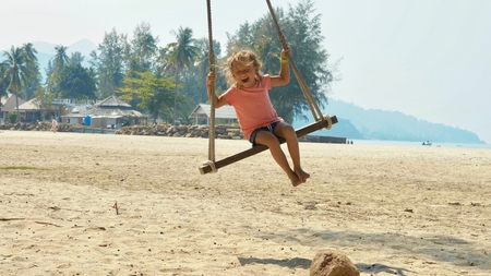 Happy laughing child girl swinging at tropical sandy beachの写真素材