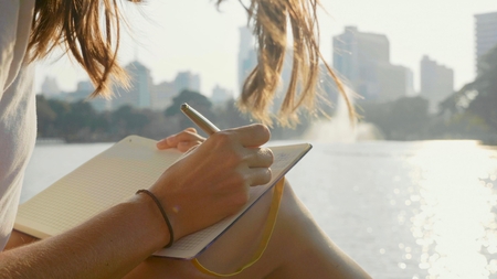 Young woman sitting on the bench in park and writing in diary, close-upの写真素材