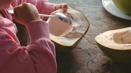 Little cute girl eating coconut by spoon at cafeの写真素材