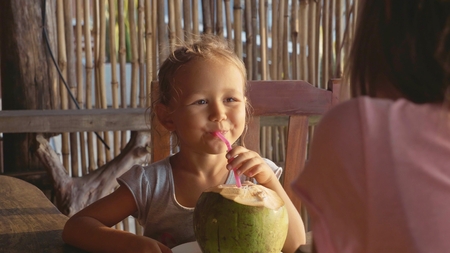 Portrait of little cute girl who sitting at cafe and drinking coconutの写真素材