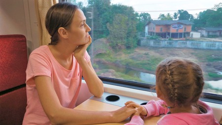 Family passing the time on train journey in Asia, looking to window and talkingの写真素材