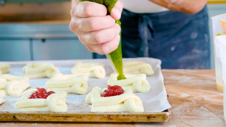 Professional baker adding jam on top of sweet baking before put it into oven