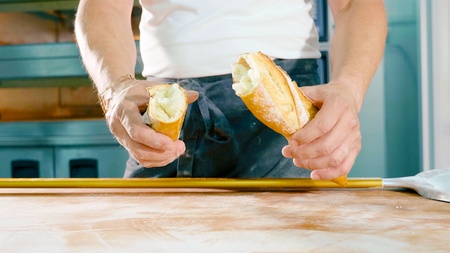 Baker tearing fresh bread on a half. Male hands holds baguetteの写真素材
