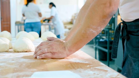 Professional baker is forming pieces of dough in bakery commercial kitchen.