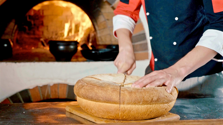 Chef cutting bread on commercial kitchen with fireplase on the background