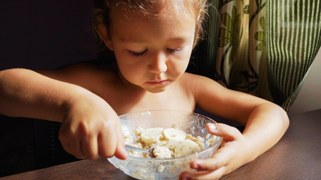 The child is having breakfast. Portrait of little cute girl eats porridge.の写真素材