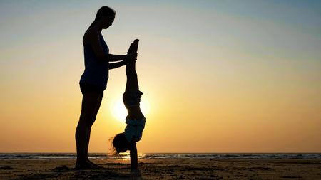 Silhouette of mother with daughter doing gymnastic on the beach at sunset