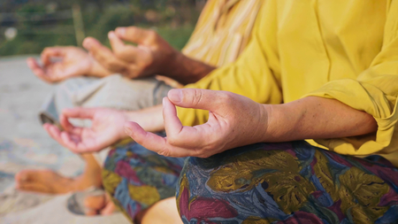 Crop of senior couple sits and meditating together on sandy beachの写真素材