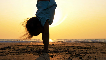Silhouette of little child girl doing gymnastic on the beach at sunset