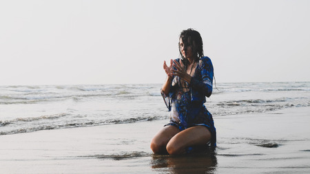 Young wet woman sitting in water at sandy beach and doing meditation practices