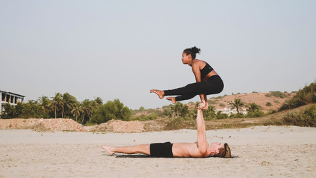 Fit sporty couple practicing acro yoga with partner together on the sandy beach.の写真素材