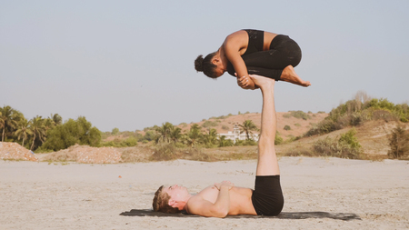 Fit sporty couple practicing acro yoga with partner together on the sandy beach.の写真素材