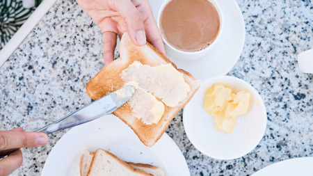 Woman is buttering toast table knife with butter making sandwich for breakfast.
