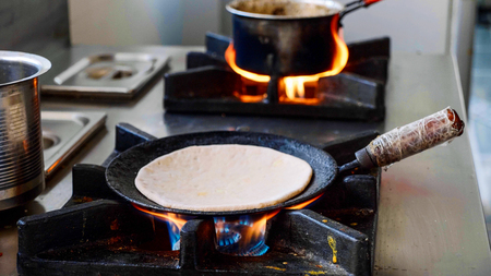 Preparing Indian aloo paratha in a frying pan on gas stove.