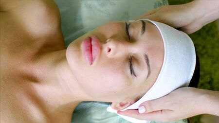 Cosmetologist puts on headband on young woman before treatment in spa salon.