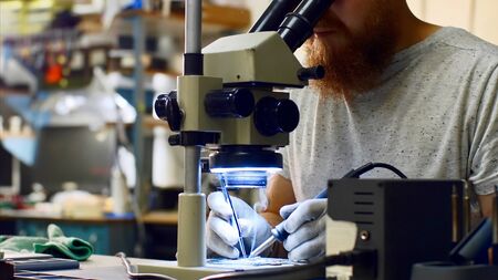 Repairman looks through microscope produces solders on circuit board of device.