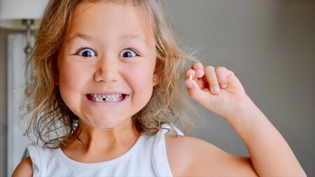 Portrait of little child girl is showing her lost milk tooth and smiling