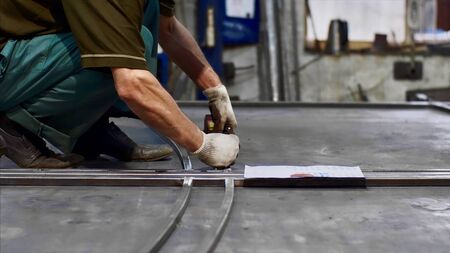 Locksmith measures tape measure length of metal bars and makes marks in workshopの写真素材