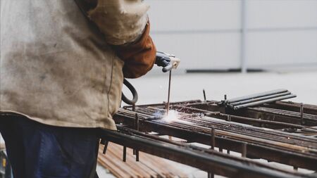 A worker is welding rebar with hollow electrode in a protective orange gloves. Sparks and smoke are...