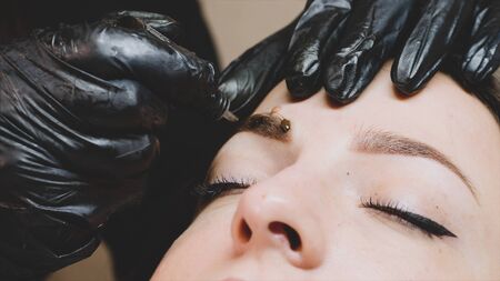 The master is adding some drops of the brown pigment on the clients eyebrow.