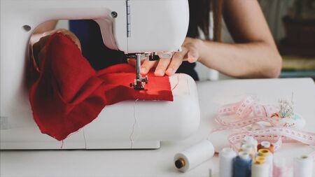 Closeup tailor woman hands sewing red cloth on sewing machine in workplace.