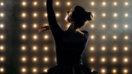 Silhouette of ballerina in black tutu is dancing ballet in the dark studio with smoke and the lights on the background.の写真素材