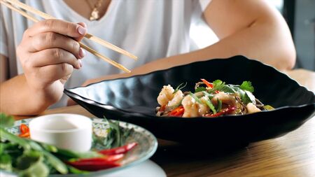 Woman eating traditional asian soba stir-fry noodles with shrimp at restaurant, close-up. Asian food concept.の写真素材