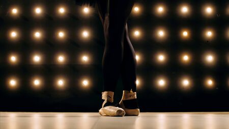 Feet of ballerina in pointe shoes is dancing ballet in the dark studio.の写真素材