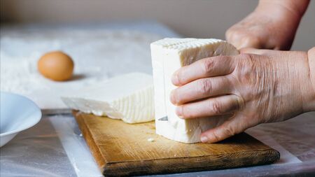 Close-up female hands is cutting a cheese for bakery preparation