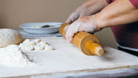 Close-up hands of senior female is rolling a dough for dumplings at home kitchen