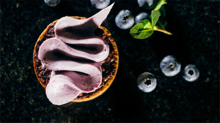 Pastry biscuit with purple cream on the table near the blueberries, close-up.の写真素材