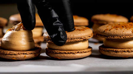 Chef is assembling caramel macarons, close-up.