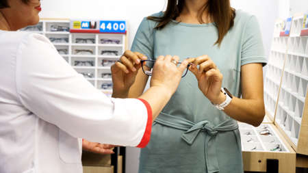 Optician is helping client to choose a spectacles in optical store.の写真素材