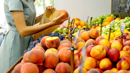 Young caucasian woman is choosing a peaches at grocery storeの写真素材