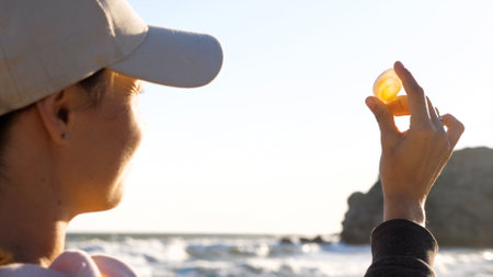 Young woman is holding seashell in hand and looking on sun through shell