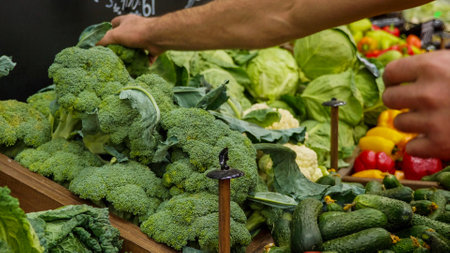 Close-up hands of grocery worker is arranging vegetables on store shelves.の写真素材