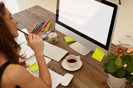 Cropped image of female designer looking at the copy space screen computer thinking about new logo for online store, keeping pencil near her mouth. High angle portrait of working designer. Mock upの写真素材