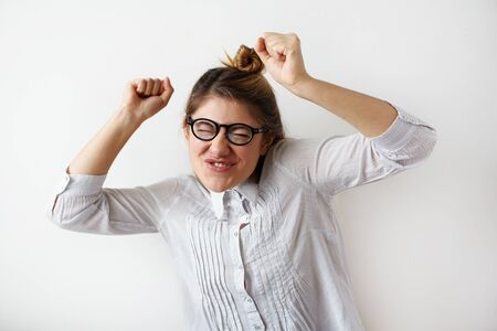 Dancing crazy girl in specturales and white striped shirt holding hands up with funny emotion on her face. Young woman listen favourite music and having positive feelings. Humorous facial expressionの写真素材