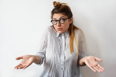 Half length portrait of frustrated attractive student female wearing formal wear anf eyeglasses holding her hands out with apologetic and confused facial emotion. Human face expressions, body languageの写真素材