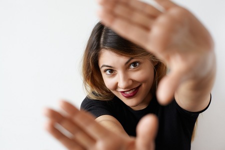 Close up portrait of pretty student female with cute smile looking at camera with happy joyful expression and gesturing hands frame on white background. Selective focus on face. Having fun conceptの写真素材