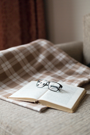 A cozy sofa, a  pillow and a plaid, open book and glasses. Leisure time, reading and resting.の写真素材