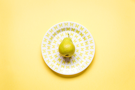 Flat lay of a ripe pear on plate, yellow paper background, summer conceptの写真素材