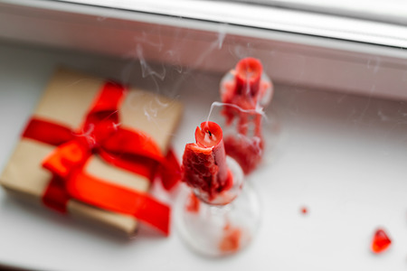 Red candles and gift-box with ribbon are on the windowsill. St. Valentines Day still- life.