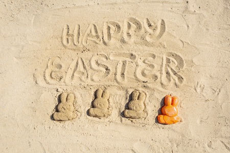 Text Happy Easter and several Easter bunnieas are on the sand.の写真素材