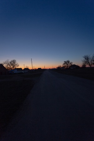 Late spring evening in the country side. Silhouettes of buildings and trees in black, blue and yellow colors. Contrast imege.の写真素材