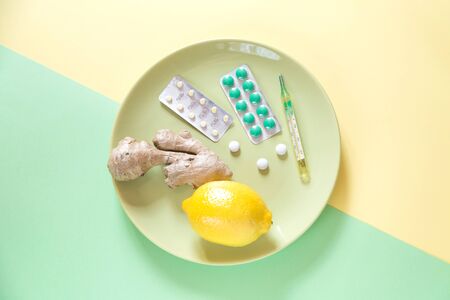 Mix of treatment on two color background. Some pills and a lemon on the plate. Green and yellow colors.の写真素材