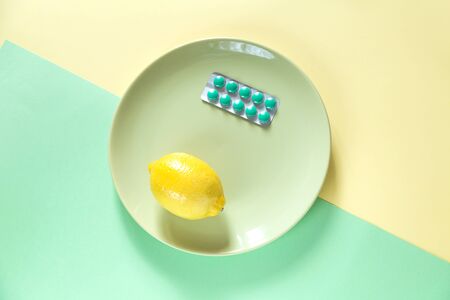 Mix of treatment on two color background. Some pills and a lemon on the plate. Green and yellow colors.の写真素材